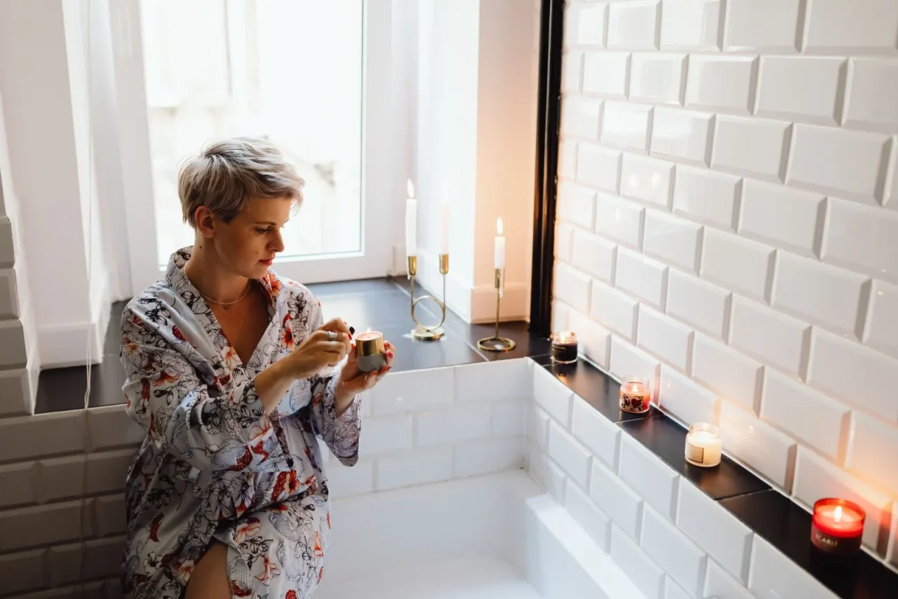 Une femme en peignoir, des bougies allumées au bord du bain