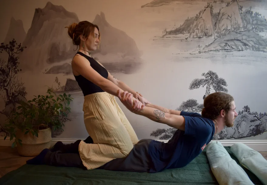 Praticienne étirant les bras d'une personne assise sur un futon, pendant un shiatsu