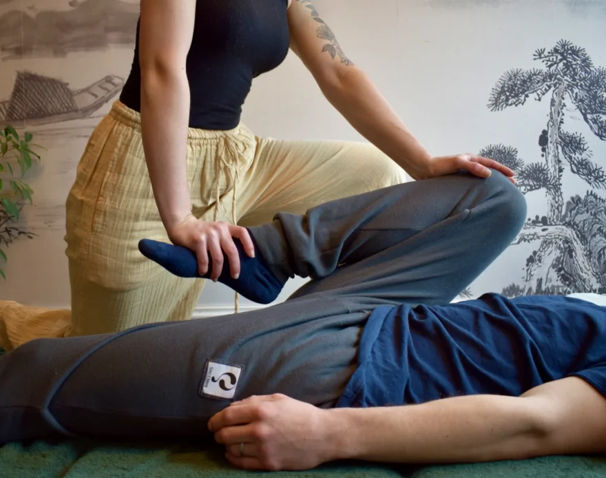Praticienne mobilisant la jambe d'une personne allongée sur un futon