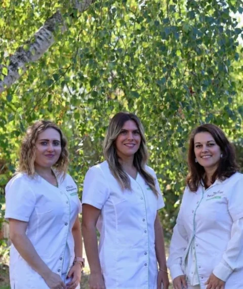 Trois praticiennes du cabinet de Royan en blouse blanche, souriantes, sous un feuillage