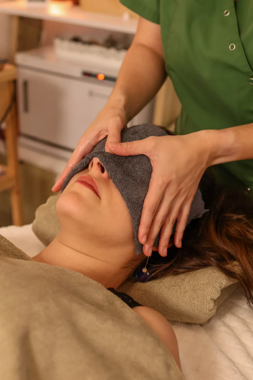 Mains d'une praticienne posées sur le front d'une cliente, un linge sur les yeux