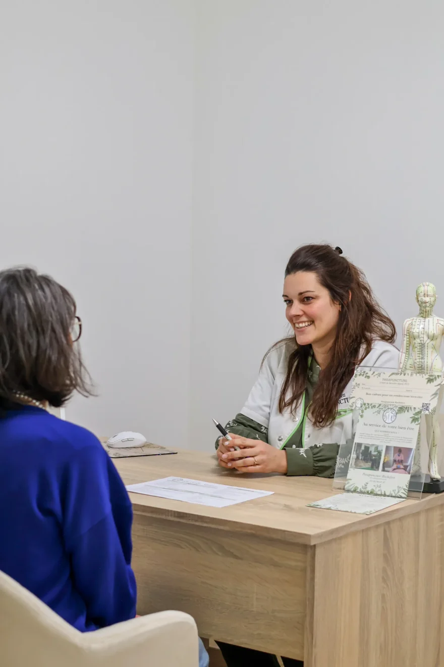 Une praticienne souriante, au bureau, face à une cliente, pendant un échange