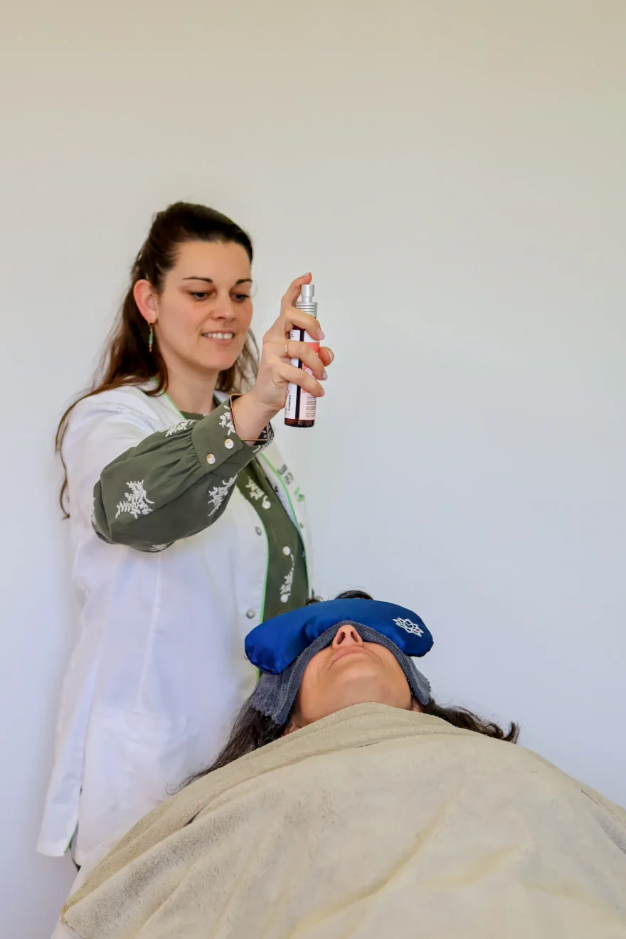 Praticienne vaporisant une brume au-dessus d'une cliente allongée, un masque de repos sur les yeux