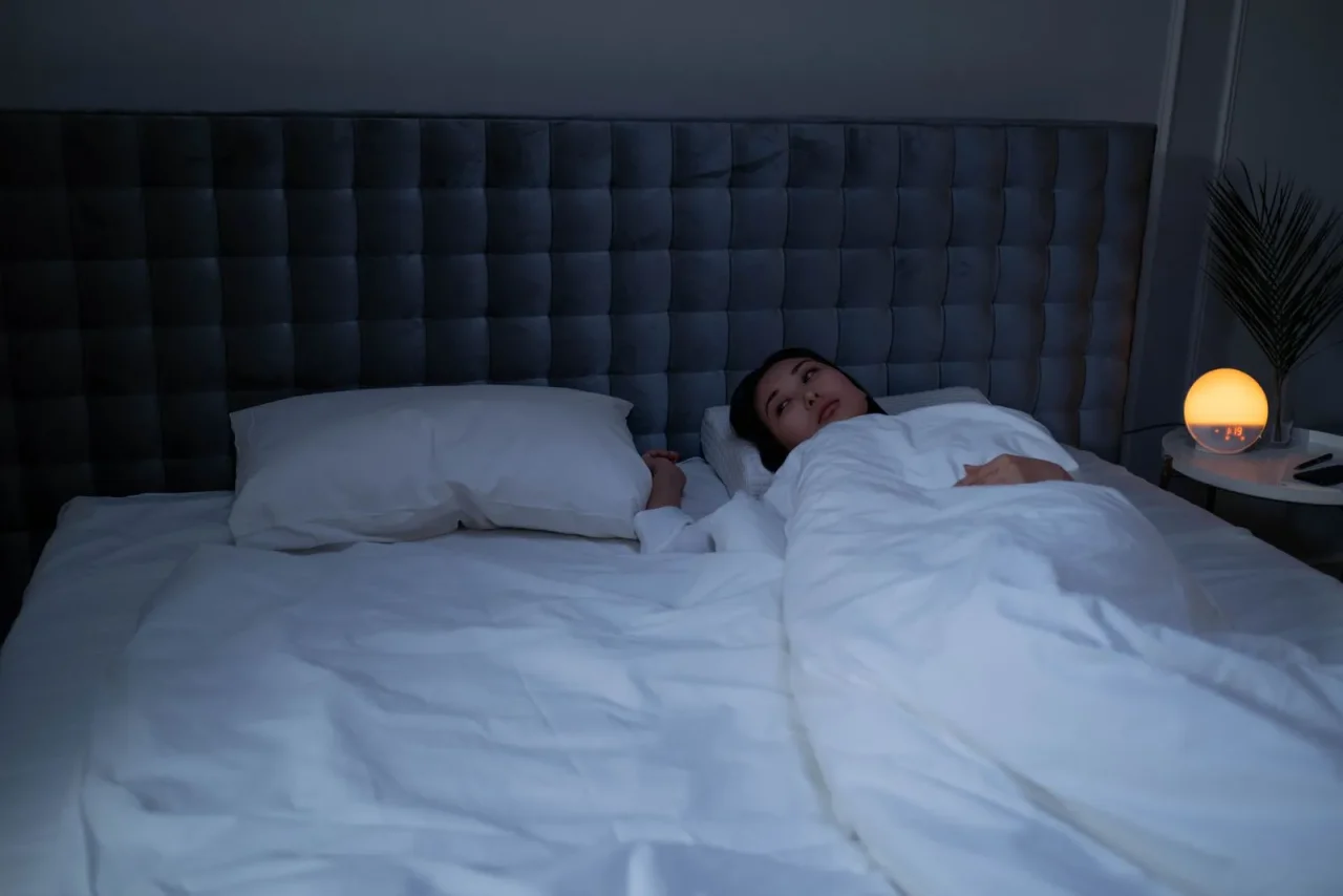 Une femme éveillée dans son lit, sous des draps blancs