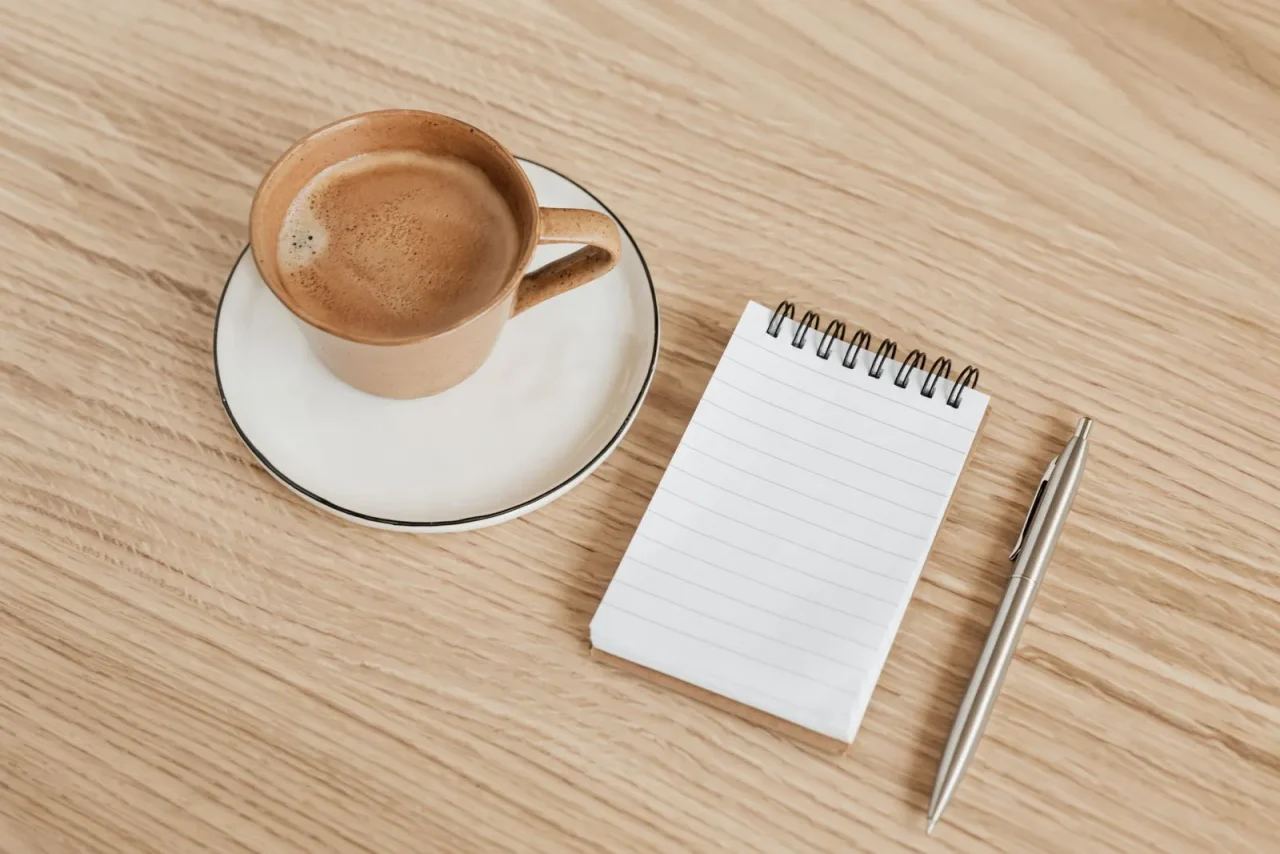 Une tasse de café, un bloc-notes vierge et un stylo sur une table en bois