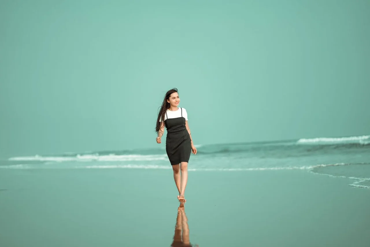Une jeune femme marche pieds nus au bord de l'eau, sur une plage, d'un pas détendu