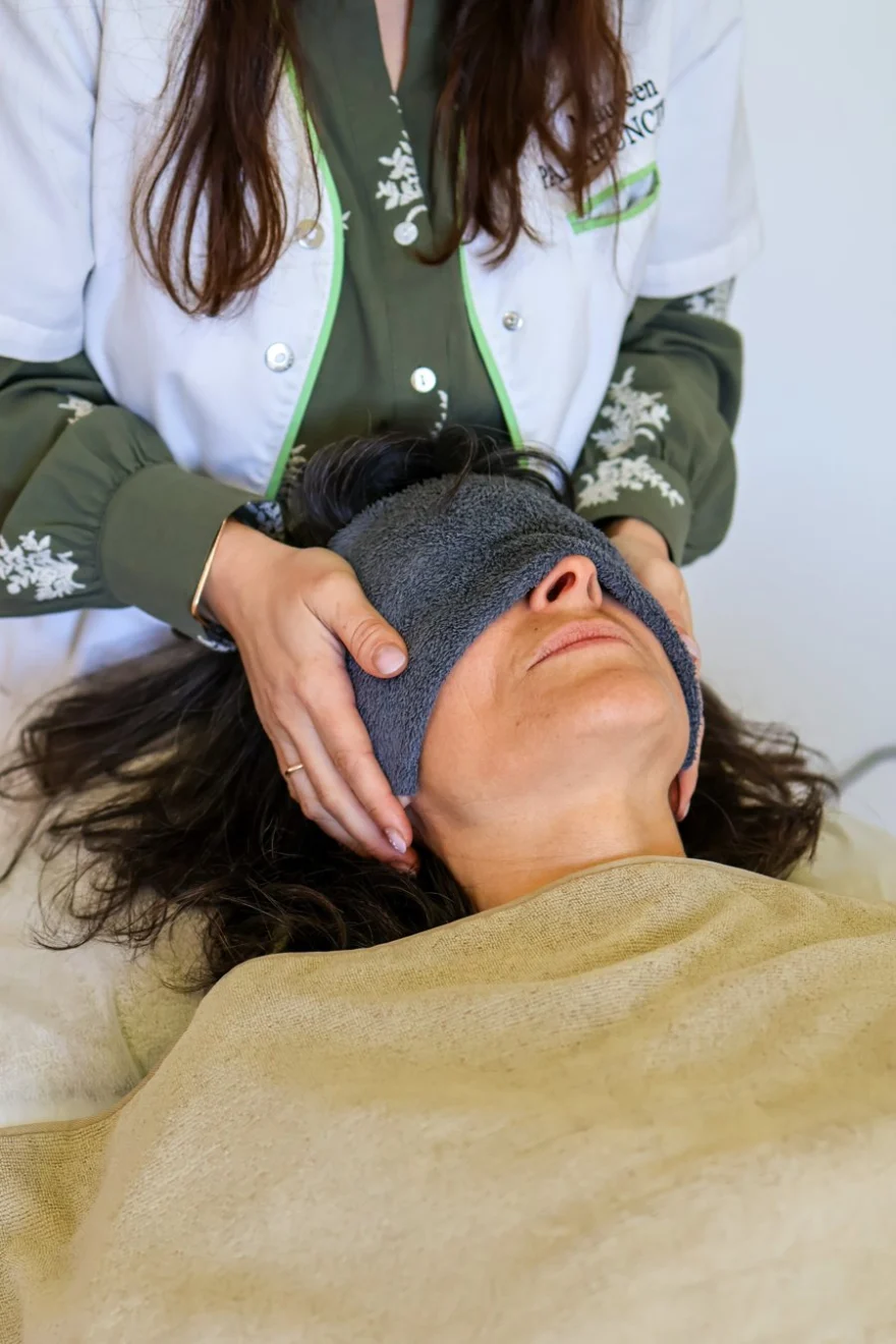 Praticienne maintenant la tête d'une cliente, un linge sur les yeux